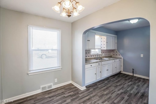 kitchen featuring arched walkways, visible vents, white cabinetry, a sink, and baseboards