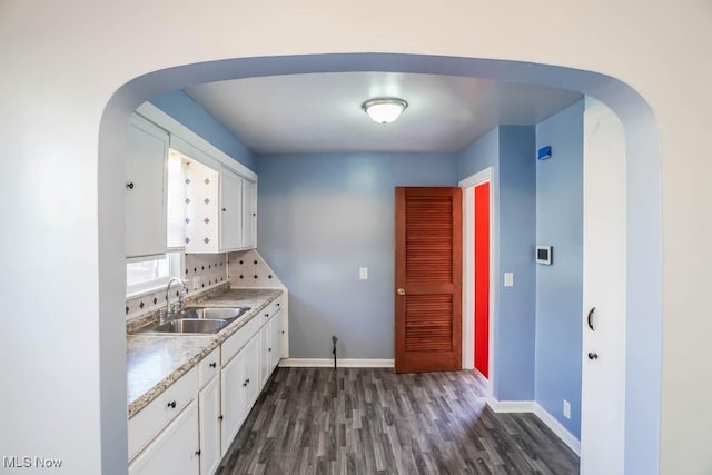 kitchen with white cabinetry, arched walkways, light countertops, and a sink