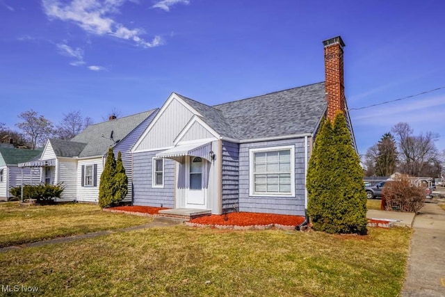 view of front facade with a shingled roof, a chimney, and a front yard