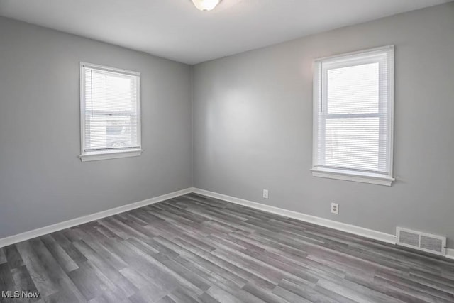 spare room with wood finished floors, visible vents, and baseboards