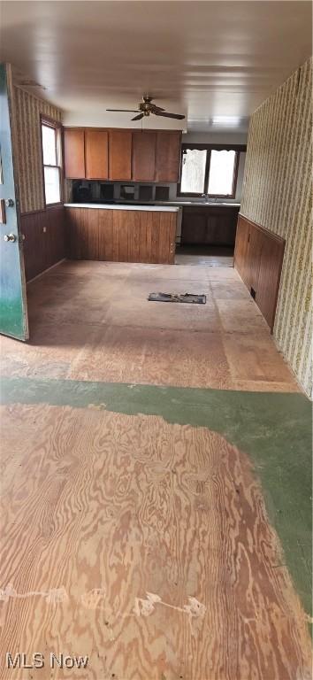 interior space with ceiling fan, brown cabinetry, and wallpapered walls