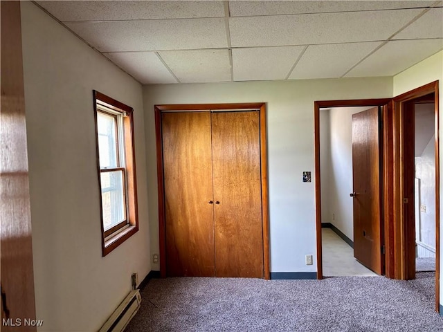 unfurnished bedroom featuring carpet, a closet, a paneled ceiling, and baseboards