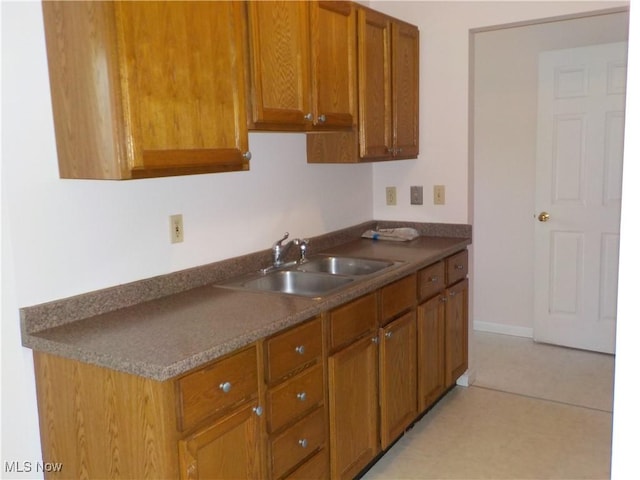 kitchen featuring brown cabinetry, light tile patterned floors, baseboards, and a sink