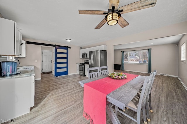 dining area featuring light wood-type flooring, visible vents, baseboards, and a barn door