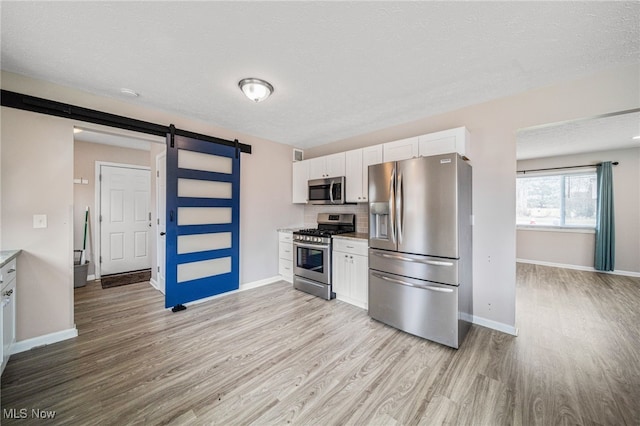 kitchen featuring stainless steel appliances, a barn door, light wood-style flooring, and white cabinetry