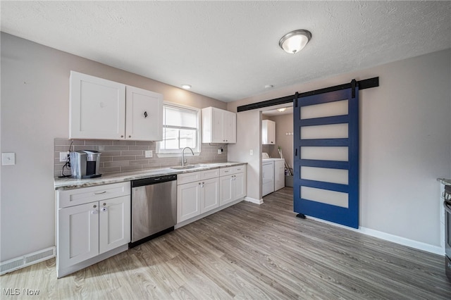 kitchen featuring a barn door, light wood-style flooring, stainless steel dishwasher, tasteful backsplash, and washer and clothes dryer