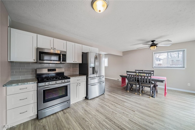 kitchen with light wood finished floors, stainless steel appliances, decorative backsplash, white cabinetry, and baseboards