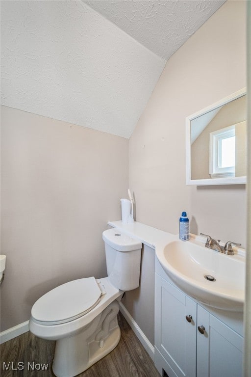 half bath featuring a textured ceiling, toilet, wood finished floors, vanity, and vaulted ceiling