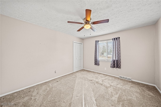 carpeted empty room with visible vents, ceiling fan, a textured ceiling, and baseboards