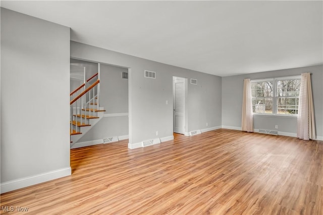 unfurnished living room featuring light wood-style floors, stairs, and visible vents