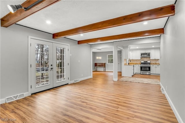 unfurnished living room with visible vents, light wood-style floors, baseboards, french doors, and beam ceiling