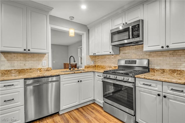 kitchen with tasteful backsplash, appliances with stainless steel finishes, light wood-style floors, white cabinets, and a sink