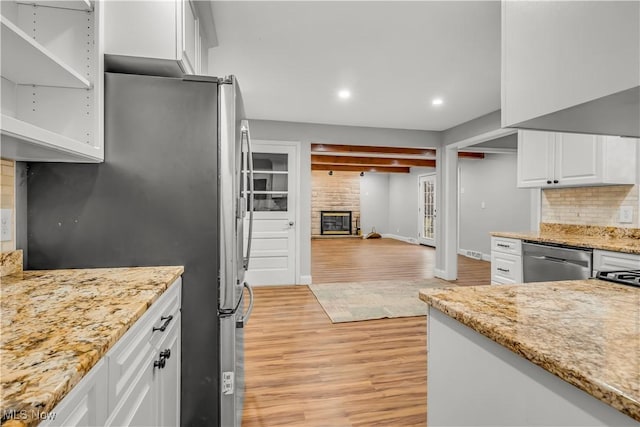 kitchen featuring a large fireplace, stainless steel appliances, white cabinetry, light wood finished floors, and tasteful backsplash