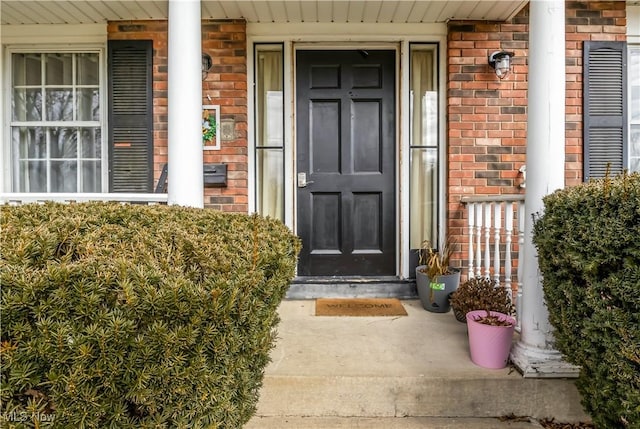 doorway to property with covered porch and brick siding