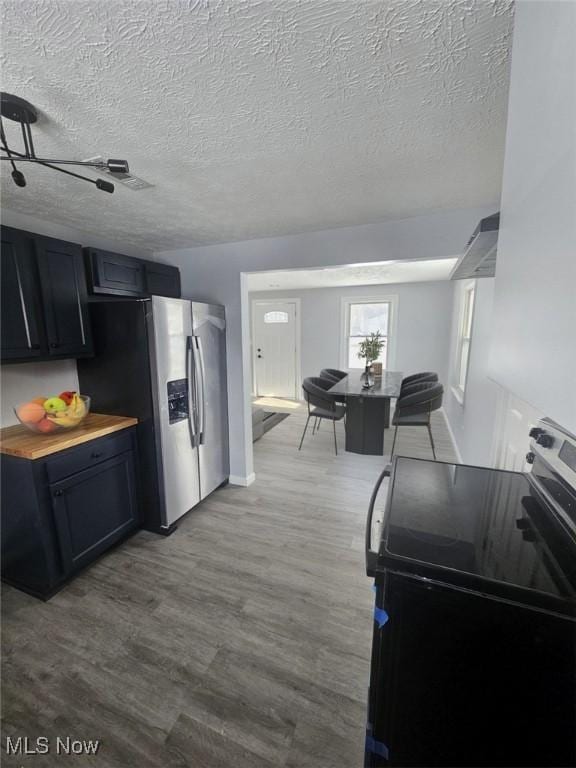 kitchen featuring wood counters, wood finished floors, stainless steel appliances, a textured ceiling, and wall chimney range hood