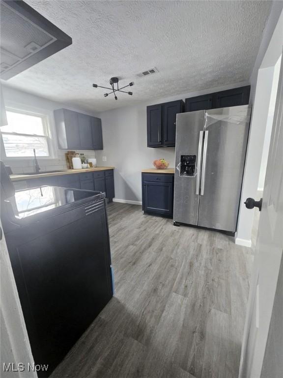 kitchen with a textured ceiling, visible vents, baseboards, light wood-type flooring, and stainless steel refrigerator with ice dispenser