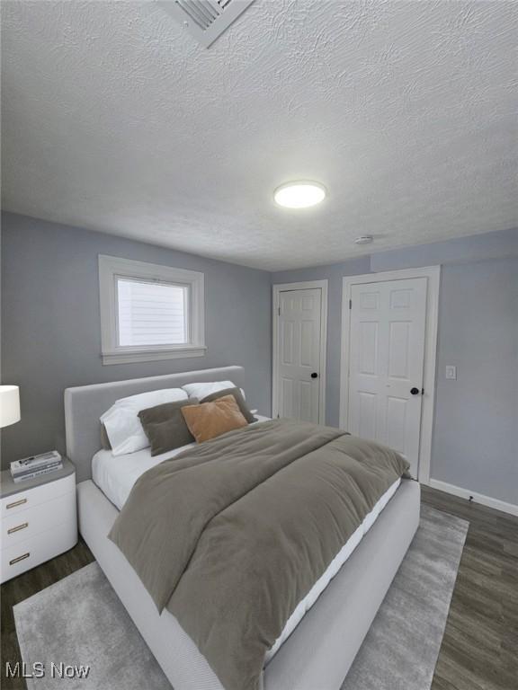 bedroom featuring visible vents, dark wood finished floors, a textured ceiling, and baseboards