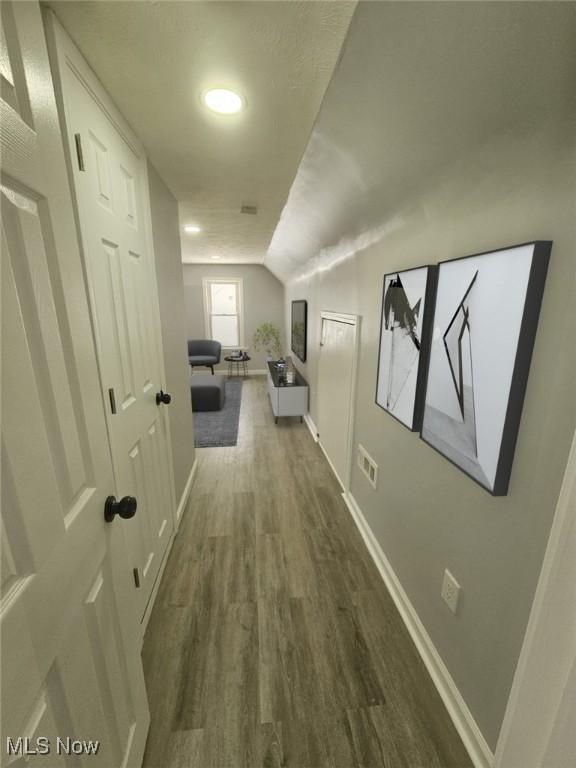 corridor with dark wood-style floors, lofted ceiling, and baseboards