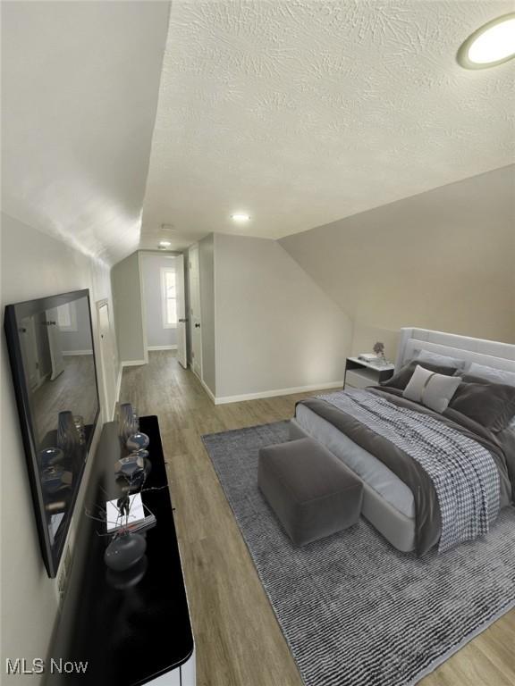 bedroom with vaulted ceiling, a textured ceiling, wood finished floors, and baseboards