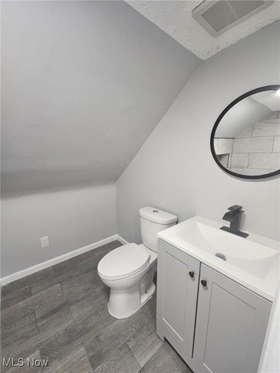 bathroom featuring lofted ceiling, visible vents, toilet, vanity, and wood finished floors