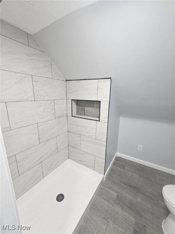 bathroom featuring vaulted ceiling, a stall shower, toilet, and baseboards