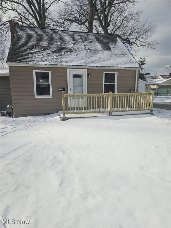 snow covered rear of property with fence and roof with shingles