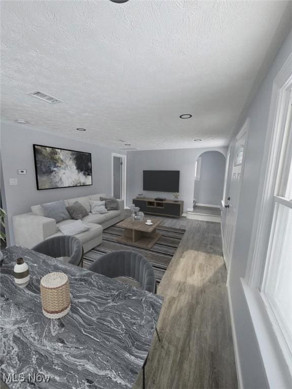 living room featuring baseboards, visible vents, arched walkways, wood finished floors, and a textured ceiling