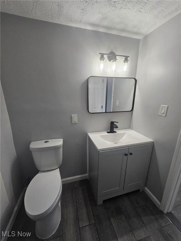 half bath with toilet, a textured ceiling, vanity, wood finished floors, and baseboards