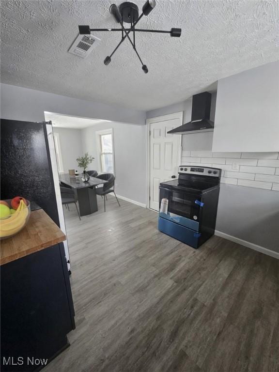 kitchen with electric stove, dark wood finished floors, butcher block counters, visible vents, and wall chimney exhaust hood