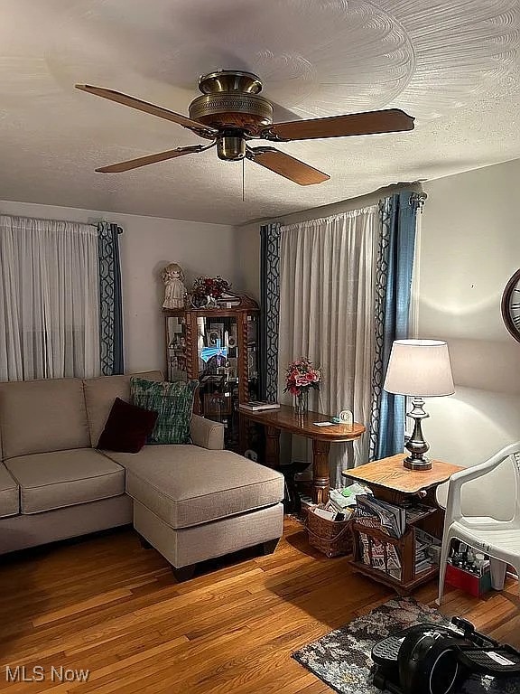 living room with a ceiling fan, a textured ceiling, and wood finished floors