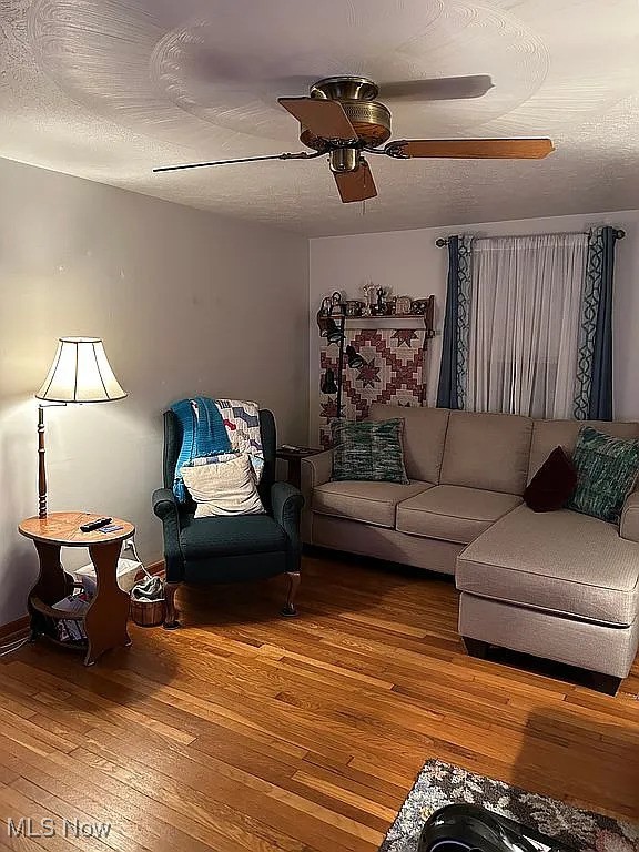 living room featuring wood-type flooring, ceiling fan, and a textured ceiling