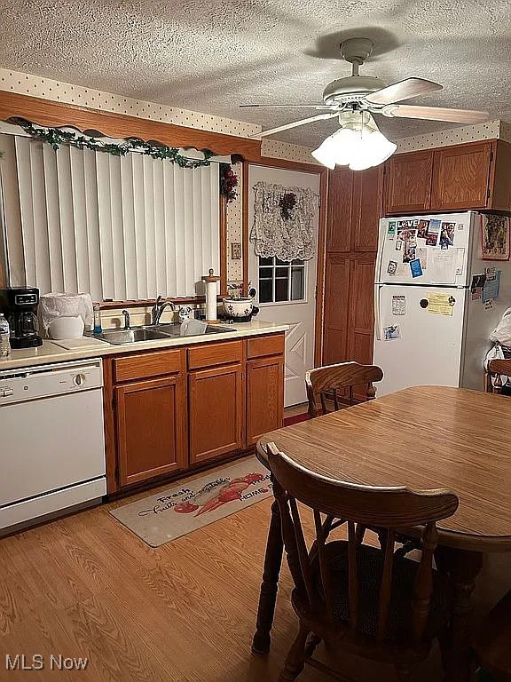 kitchen with a textured ceiling, light wood-style flooring, white appliances, a sink, and brown cabinets