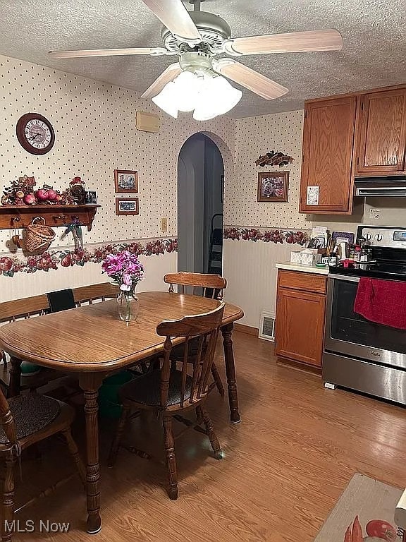 dining space featuring light wood-style flooring, arched walkways, a textured ceiling, and wallpapered walls