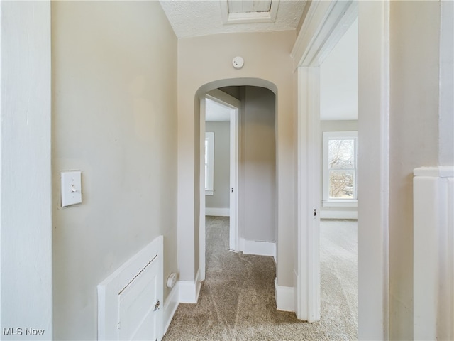 hall featuring arched walkways, light colored carpet, and baseboards