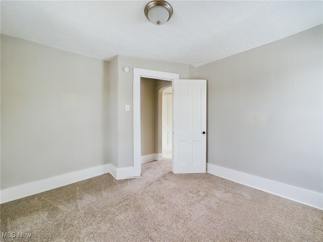 unfurnished room with light carpet, baseboards, and a textured ceiling