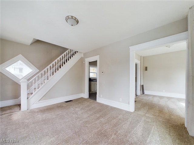 unfurnished living room with carpet floors, visible vents, and stairway