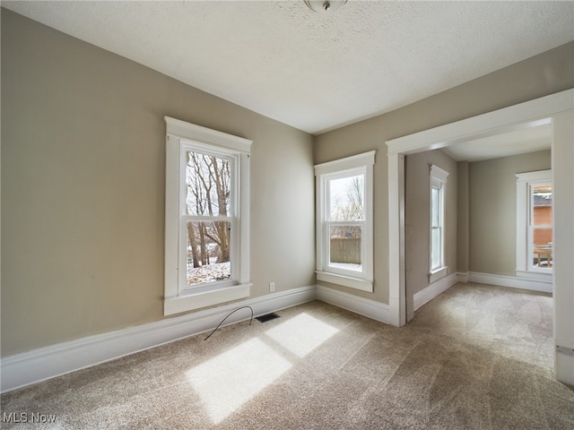 carpeted empty room featuring visible vents, a textured ceiling, and baseboards