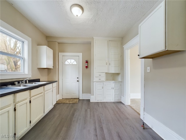 kitchen with wood finished floors, dark countertops, a sink, and baseboards