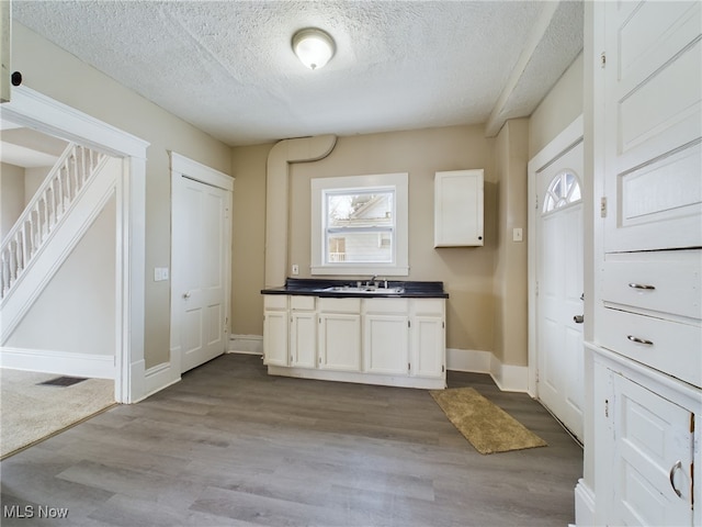 kitchen featuring dark countertops, white cabinetry, dark wood finished floors, and a sink