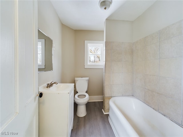 bathroom with toilet, wood finished floors, vanity, baseboards, and a bath