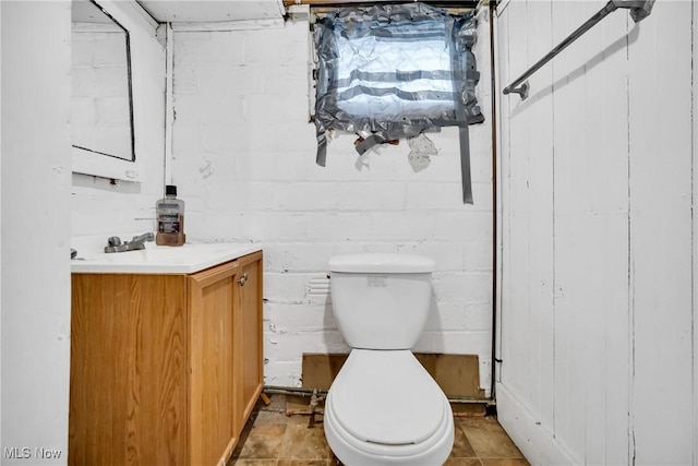 half bath with concrete block wall, vanity, and toilet