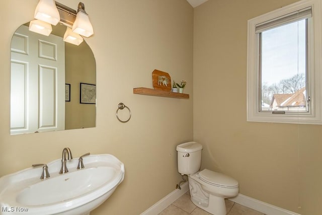 half bathroom featuring tile patterned flooring, a sink, toilet, and baseboards