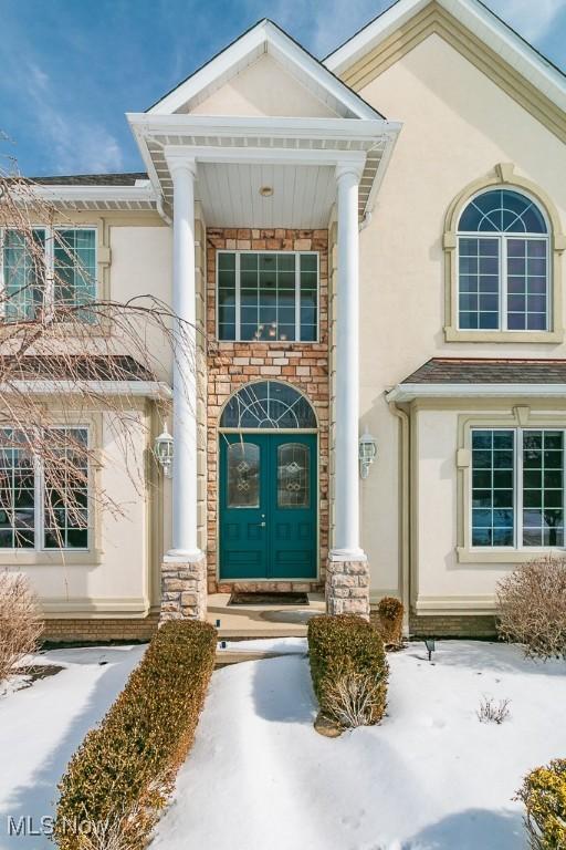 snow covered property entrance with stone siding and stucco siding