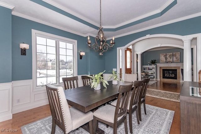 dining space featuring a raised ceiling, wainscoting, wood-type flooring, and a glass covered fireplace