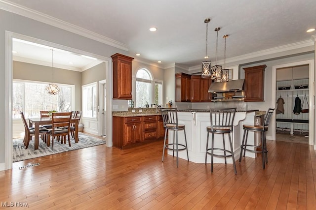 kitchen featuring a breakfast bar, pendant lighting, a notable chandelier, under cabinet range hood, and hardwood / wood-style floors