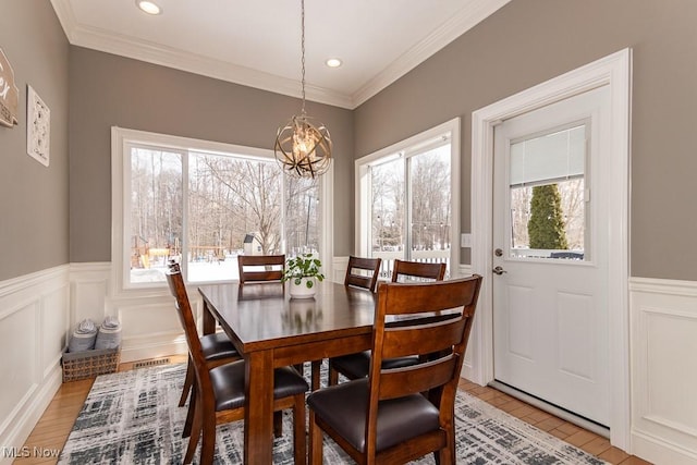 dining area featuring light wood-type flooring, ornamental molding, a decorative wall, and a notable chandelier