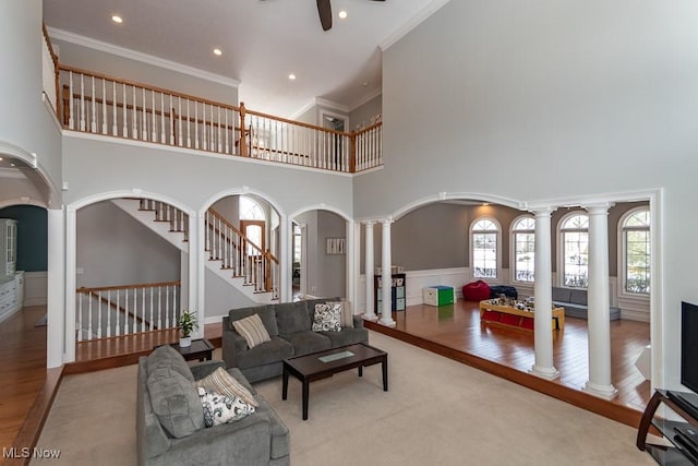 living area with decorative columns, arched walkways, wood finished floors, and ornamental molding