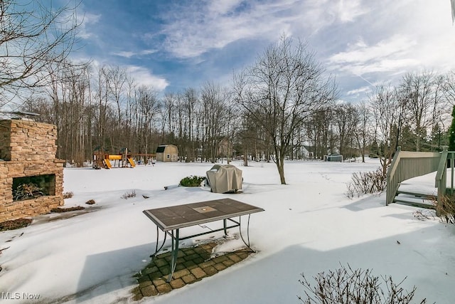 yard layered in snow featuring an outbuilding, an outdoor stone fireplace, and a patio area