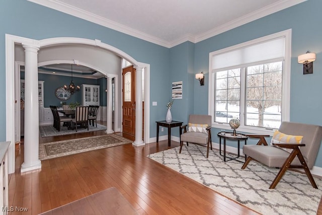 living area with decorative columns, arched walkways, ornamental molding, hardwood / wood-style floors, and a notable chandelier