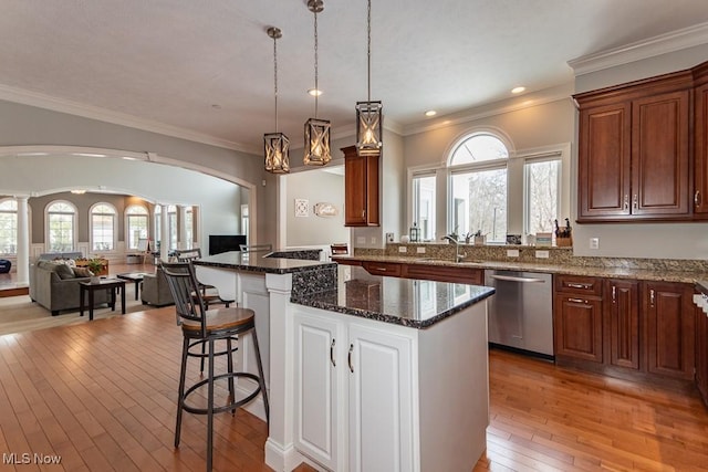 kitchen featuring arched walkways, light wood finished floors, stainless steel dishwasher, open floor plan, and a kitchen bar